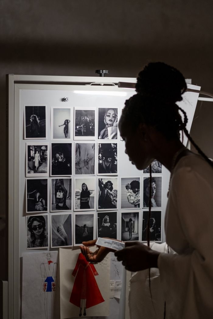 A silhouette of a fashion designer examining a creative mood board filled with fashion sketches and photos.